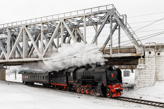 old black steam locomotive in Russia in the winter on a background of bridge