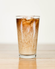 Iced coffee on a wood table with cream being poured into it showing the refreshing drink with a clean background