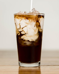 Iced coffee on a wood table with cream being poured into it showing the refreshing drink with a clean background