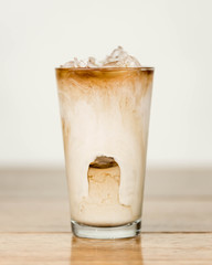 Iced coffee on a wood table with cream being poured into it showing the refreshing drink with a clean background