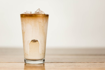 Iced coffee on a wood table with cream being poured into it showing the refreshing drink with a clean background