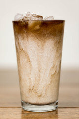 Iced coffee on a wood table with cream being poured into it showing the refreshing drink with a clean background