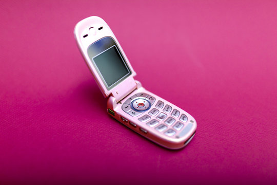 Cool and classic pink retro flip cell or mobile phone isolated against a red background