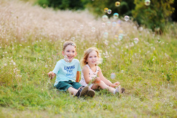 Naklejka na ściany i meble children - a boy and a girl are sitting in the grass and blowing bubbles