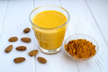 Almond milk with turmeric on the white wooden background