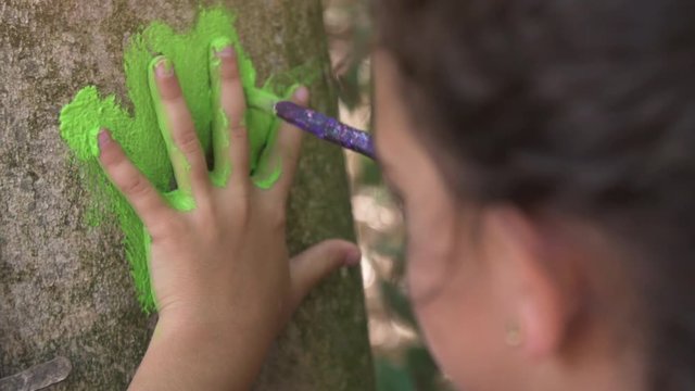 Happy young girl in summer camp leaving handprints with colorful paint on trees art outside kids playing outdoor in park under trees slow motion