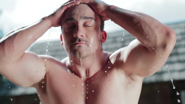 Young shirtless muscular guy freshening up with cool water out of the wooden bucket. Cool down, healthy lifestyle, strongman