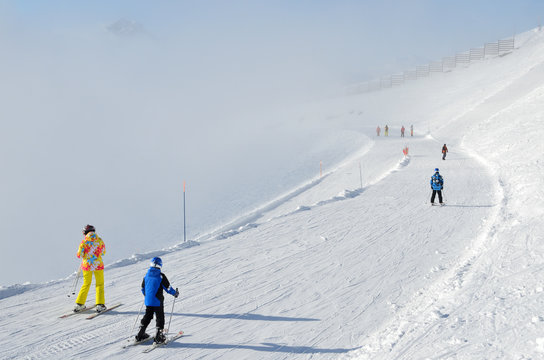 Сочи, горнолыжный курорт Роза Хутор. Лыжники в яркой спортивной одежде спускаются с горнолыжной трассы "Горицвет" в условиях ограниченной видимости