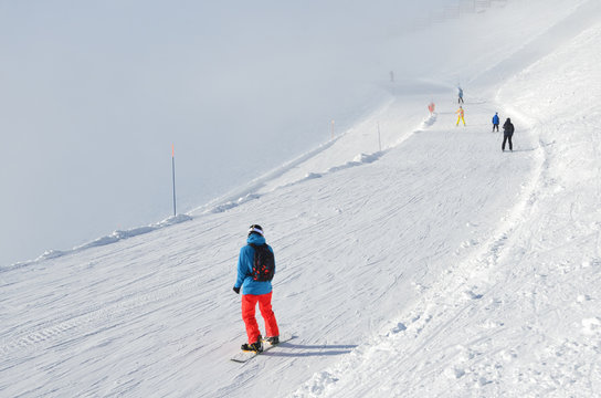 Сочи, горнолыжный курорт Роза Хутор. Сноубордист в яркой спортивной одежде спускаются с горнолыжной трассы "Горицвет" в условиях ограниченной видимости