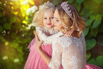 Loving mom hugs her daughter in the park. Princess in pink dresses