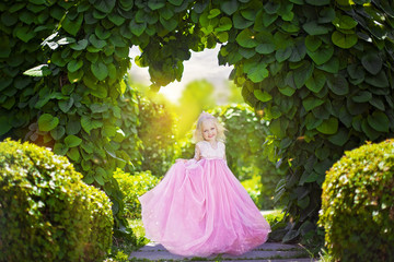 Beautiful little princess in pink dress on background of green arch in the park © popovatetiana