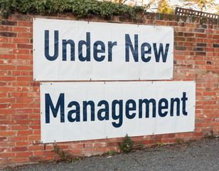 big large white and black sign on brick wall under new management