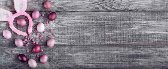 Easter eggs in a fashionable coloring on a gray wooden background with a female hoop with Easter bunny ears