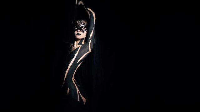 Gothic girl in a mask stands in the dark gracefully holding up her hand