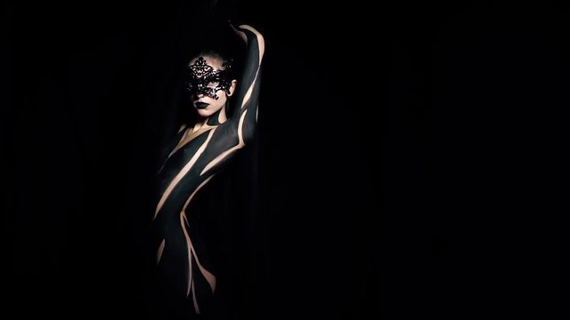 Slender gothic naked woman in black body art posing in a mask