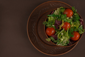 Fresh salad closeup - arugula, iceberg, cherry tomatoes, chinese and red cabbage in brown dish