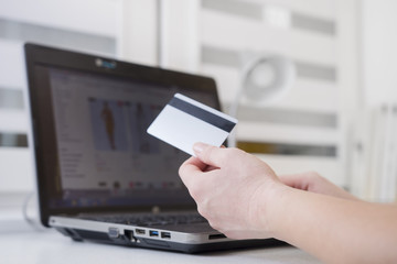 Plastic credit card in hand of woman against internet catalog on display of laptop. Online payments concept. Ordering shopping on-line.