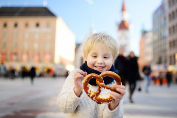 Little tourist holding traditional bavarian bread called pretzel on the town hall building background in Munich, Germany