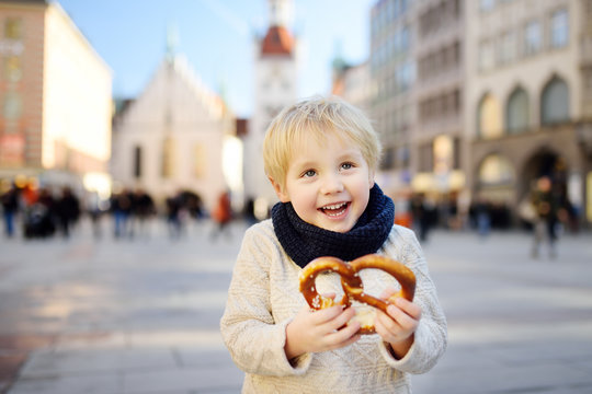 Little tourist holding traditional bavarian bread called pretzel on the town hall building background in Munich, Germany