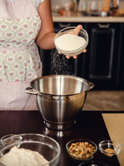 Female hand pour sugar into a big metal bowl for making a dough. Home cooking on kitchen.