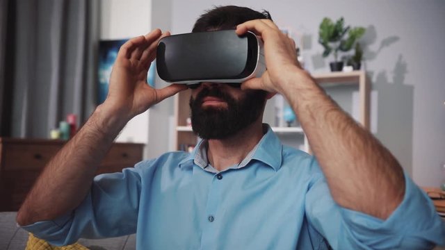 Close up face young man wearing virtual reality glasses waving his hands sit on the sofa home feel shock innovation looking modern entertainment gadget new tech visual beard game hipster slow motion
