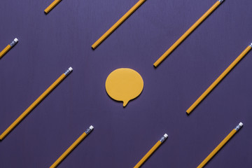 Speech bubble surrounded by wooden pencils -
 Communication concept with a post-it note, in shape of a speech bubble, surrounded by aligned orange pencils with erasers, on a purple background.