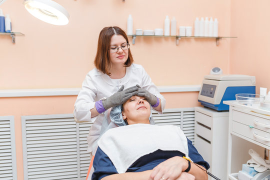 Woman doctor doing facial massage with electric gloves in cosmetology clinic