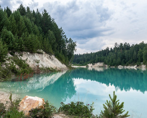 High white bank of the blue pond overgrown with spruces