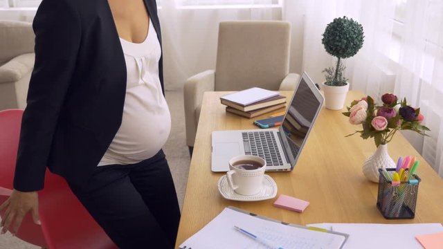 Serious pregnant businesswoman drinking tea and starts working on laptop
