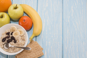 Healthy Breakfast. Oatmeal with raisins in white bowl. Two green apples, bananas. Flat top view.