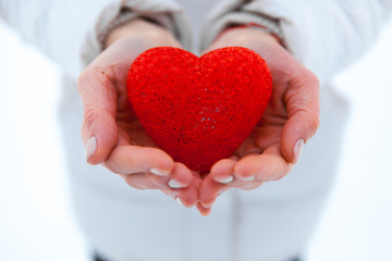 The red textured heart lies on the palms. Valentine's Day.