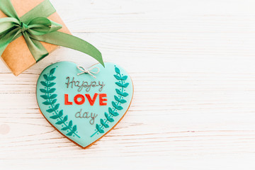 happy valentine's day greeting card. happy love day text on cookie heart and craft gift box with green ribbon on white rustic wooden background with confetti flat lay. space for text . mock-up