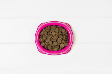 Dry dog pet food in bowl on white wooden background top view. Pet feeding concept backgrounds with copy space. Photograph taken from above.