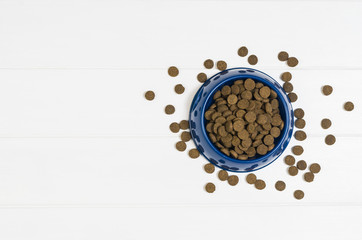 Dry dog pet food in bowl on white wooden background top view. Pet feeding concept backgrounds with copy space. Photograph taken from above.