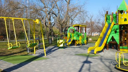 A roundabout spinning and wooden swings sways in an empty playground
