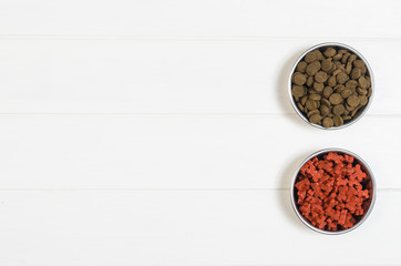 Dry dog pet food in bowl on white wooden background top view. Pet feeding concept backgrounds with copy space. Photograph taken from above.
