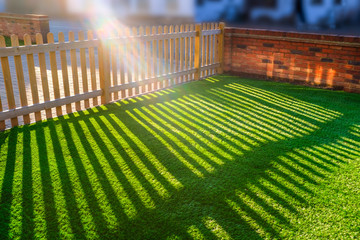 sun shining through a wooden picket fence onto an artificial grass lawn