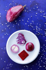 Purple cabbage, onions and beetroot on a white plate, vegetables in space, vegetables on the ultraviolet background, coarse salt, purple onions, purple eggplant on a dark blue background, pop art