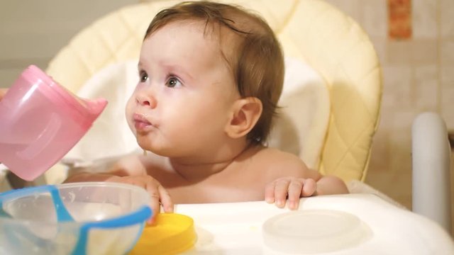 mother gives to drink water of baby after feeding. child drinks water at table