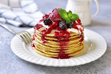 Stack of homemade delicious vanilla pancakes topped with sour cream,rasbberry syrup and berries.