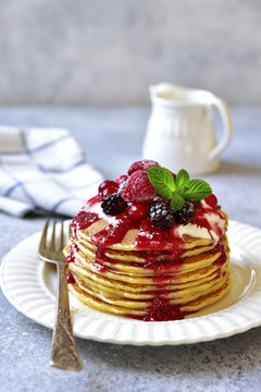 Stack of homemade delicious vanilla pancakes topped with sour cream,rasbberry syrup and berries.