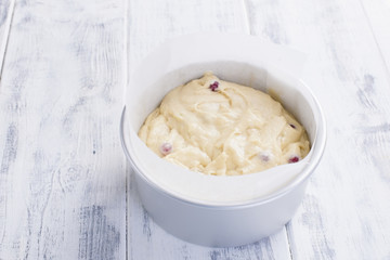 Red berries in a dough for a home-made pie. In a steel bowl. White wooden background and free space for text.