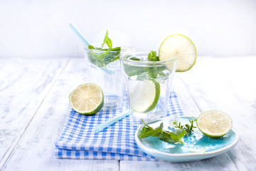 Two glasses of water and fresh green mint, and lime. On a blue napkin on a wooden background. free space for text or a postcard.