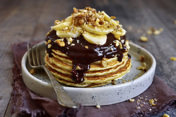 Stack of homemade delicious banana pancakes topped with chocolate sauce, banana slices and walnut.