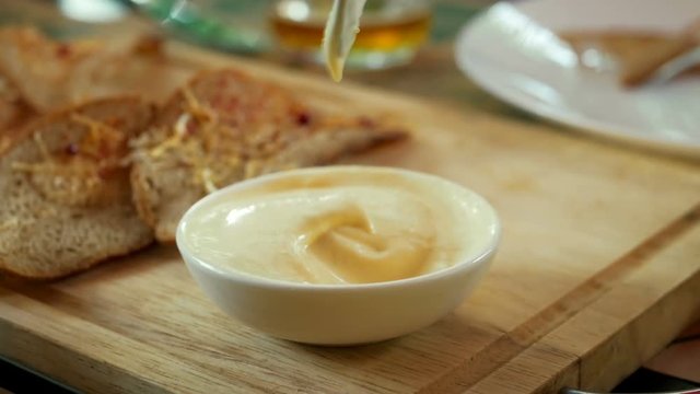 Toasts from rye bread and cheese dips into garlic sauce in bar as snack for beer party in a cheerful company of friends. Spoon mixes the sauce