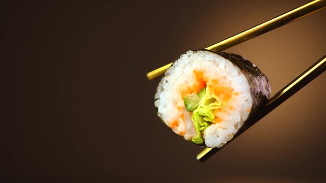 Sushi roll in chopsticks over black background. Seafood. Healthy eating, dieting concept. 4K UHD video footage. 3840X2160