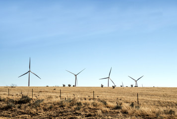 Large white wind turbines in a fenced pasture in a brown barren spring time countryside landscape
