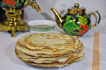 close-up of large and small pancakes lie on a plate, on the background of colorful samovar and kettle.