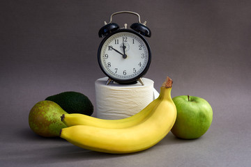 Alarm clock, fruits and toilet paper on a blue background. Natural remedy for constipation