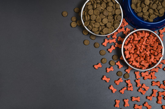 Dry dog pet food in bowl on blach chalkboard background top view. Pet feeding concept backgrounds with copy space. Photograph taken from above.